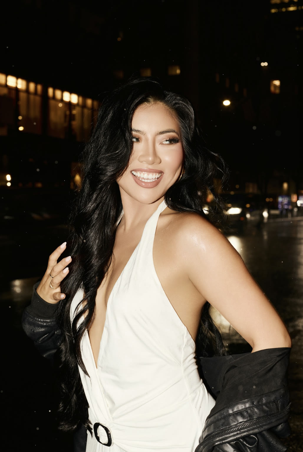 Vivian True smiling with a leather jacket draped over her arm on a city street at night