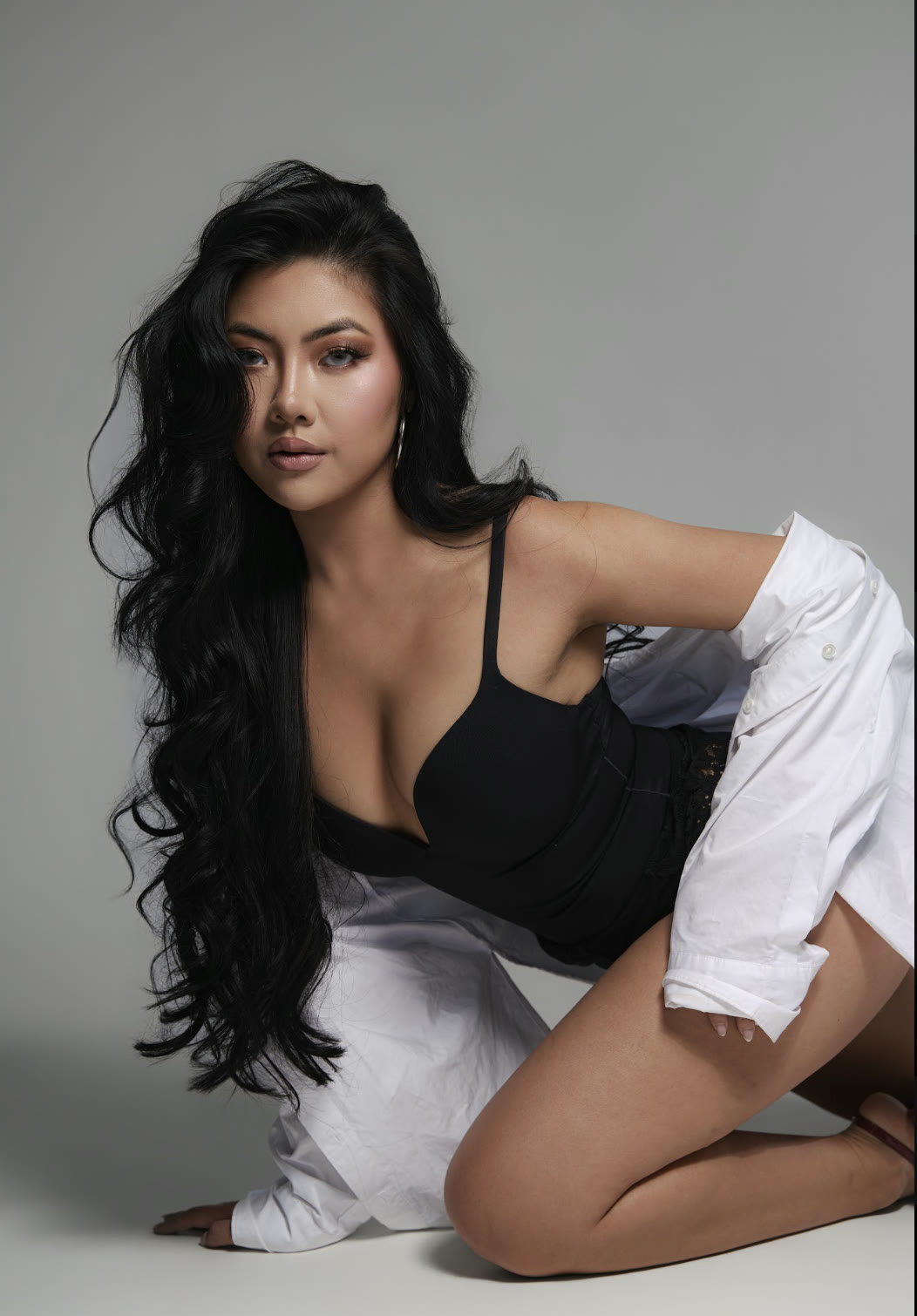 Vivian True kneeling in a black top and white oversized shirt, studio portrait